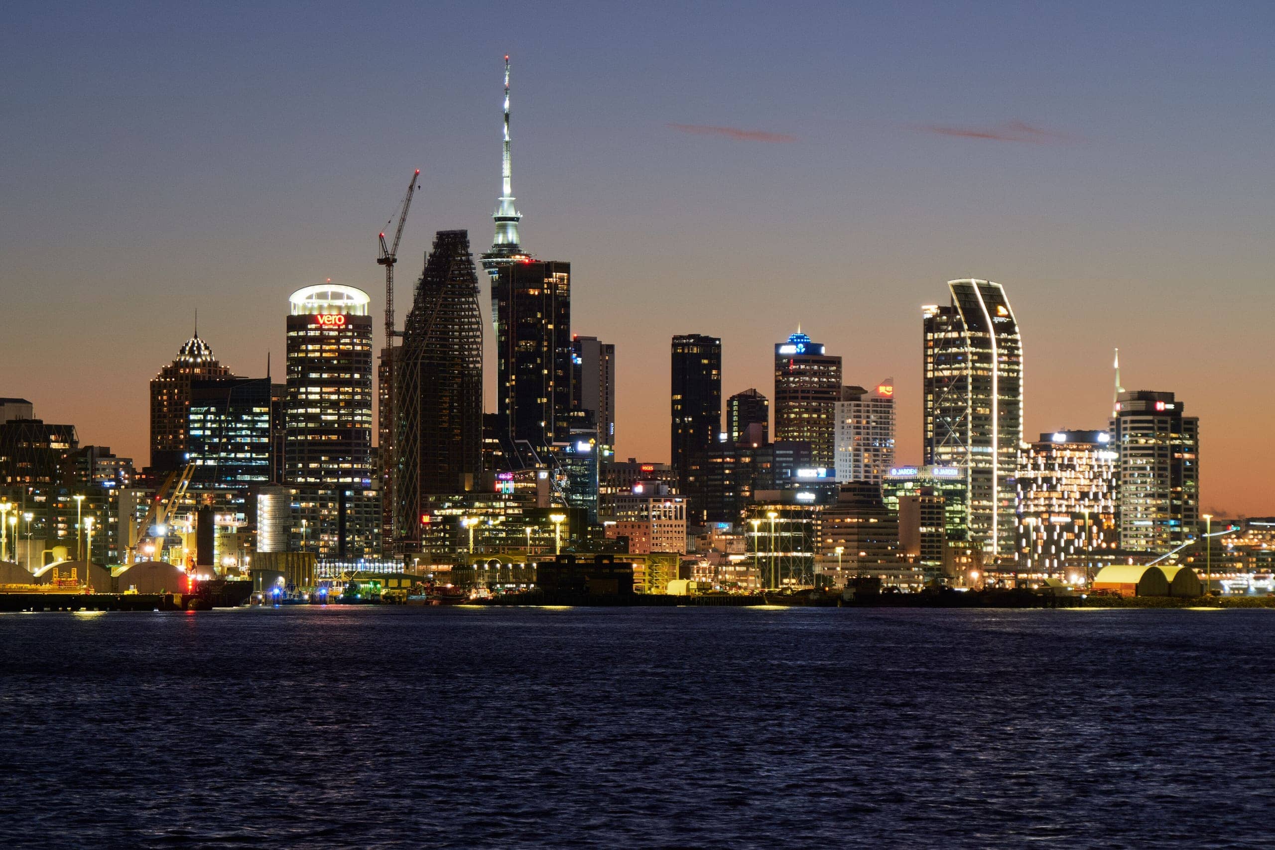 Auckland skyline and Sky Tower lit up across the Waitemata Harbour at dusk